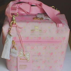 May include: A light pink soft cooler bag featuring a floral pattern, gold hardware, and a pink adjustable shoulder strap. The front displays the Stanley and LoveShackFancy logos, a zippered pocket, and a product tag labelled Julienne Mini Soft Cooler.