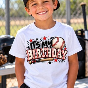 May include: A white short-sleeved t-shirt featuring a graphic design with a baseball, a wooden baseball bat, and the text "IT'S MY BIRTHDAY" in a baseball-stitched font, accented with red and black stars and motion lines.