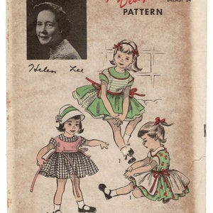 May include: A vintage sewing pattern envelope featuring illustrations of three children wearing dresses. One child wears a green and white striped dress, another a pink and black gingham dress with a hat, and the third a green dress with red cherry prints.