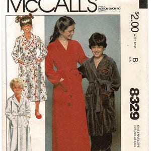 May include: A McCalls 8329 sewing pattern envelope featuring illustrations of three different robe styles. One robe has a strawberry print, one is solid red, and one is dark gray with red trim. The text includes McCalls, 8329, and Norton Simon Inc.