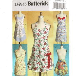 May include: A Butterick sewing pattern, B4945, featuring various apron designs. Aprons include floral, cherry, and patterned prints. The pattern includes a range of sizes from small to large. The aprons are displayed on dress forms.