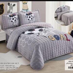 May include: A four-piece bedspread set in grey featuring a soccer ball pattern and the word GOAL in large letters. The set includes a quilted bedspread, a fitted sheet, and two pillow shams, all decorated with soccer-themed graphics and motifs.