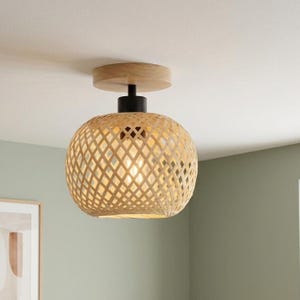 Peut inclure: Un plafonnier encastré doté d'un abat-jour arrondi en bambou tressé avec un motif en losange. Le luminaire comprend une plaque de base circulaire en bois clair et une douille en métal noir mat reliant l'abat-jour au plafond.