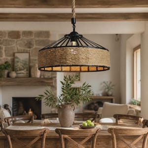 Può includere: Una lampada a sospensione con una struttura circolare in metallo nero avvolta da una spessa corda di juta naturale. L'apparecchio è sospeso tramite un cavo in corda abbinato e contiene una lampadina visibile nella struttura metallica.