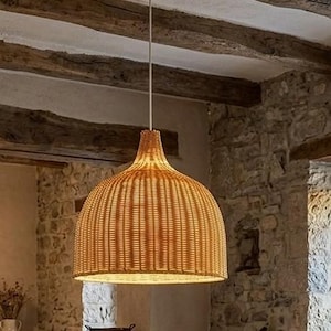 Peut inclure: Une suspension en forme de dôme fabriquée en rotin tressé de couleur brun clair. La lampe présente un motif de tissage vertical serré et est suspendue par un cordon blanc unique, créant un aspect texturé et chaleureux pour l'éclairage.