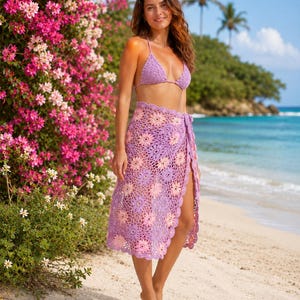 May include: A lavender crochet bikini top and a matching lavender and light pink crochet sarong skirt featuring a floral motif pattern with a scalloped edge. The skirt is designed as a wrap-around style with a tie closure at the side.