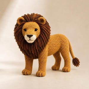 Puede incluir: Un león de ganchillo hecho a mano con un cuerpo de color amarillo dorado y una melena espesa de hilo marrón oscuro. El león tiene orejas pequeñas y redondeadas, ojos de cuentas negras, una nariz bordada en marrón oscuro y una cola larga.