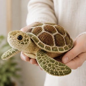 Puede incluir: Un juguete de tortuga marina tejido a ganchillo con un caparazón texturizado en tonos marrón y crema, una cabeza de color tostado claro con detalles en verde oscuro y un ojo de plástico negro. El cuerpo presenta puntadas de hilo detalladas.