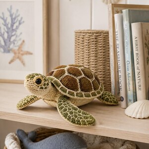 Pu&ograve; includere: Un peluche a forma di tartaruga marina realizzato all'uncinetto con un guscio esagonale testurizzato marrone e verde, testa e ventre beige chiaro e occhi scuri. La tartaruga presenta pinne dettagliate con motivi verdi e beige.
