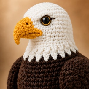 Puede incluir: Un juguete de peluche de águila calva hecho a ganchillo con cabeza blanca, cuerpo marrón oscuro y un pico ganchudo de color amarillo brillante. El águila tiene un ojo oscuro y brillante visible con iris dorado, tejido con puntadas de hilo.