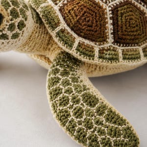 Pu&ograve; includere: Un giocattolo a forma di tartaruga realizzato all'uncinetto con un guscio dettagliato nei toni del marrone e del verde, accentuato da cuciture color crema. La testa e le pinne presentano un motivo testurizzato verde oliva e crema lavorato.