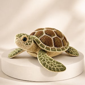 Pu&ograve; includere: Un peluche a forma di tartaruga marina realizzato all'uncinetto, con un guscio testurizzato caratterizzato da motivi geometrici marroni e verdi. La testa e le pinne sono in filato beige chiaro con accenti verdi e un occhio nero.