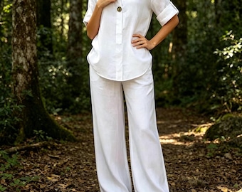 Pode incluir: Um conjunto de duas peças branco composto por uma camisa de manga curta com decote em V, um botão visível e mangas com bainha, combinado com calças largas a condizer. O conjunto é de cor branca sólida e tem um corte descontraído.