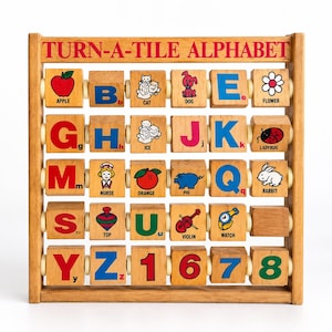 May include: A wooden Turn-A-Tile Alphabet learning toy featuring five horizontal rows of rotating square blocks. Each block displays a letter, number, or colorful illustration with corresponding text, including an apple, cat, dog, flower, ice, ladybug, nurse, orange, pig, rabbit, top, violin, and watch.