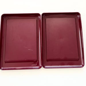 May include: Two rectangular, deep-maroon plastic trays with rounded corners and a raised central panel. Each tray features a smooth, glossy finish and a distinct border edge, presenting a uniform design suitable for organization or display purposes.