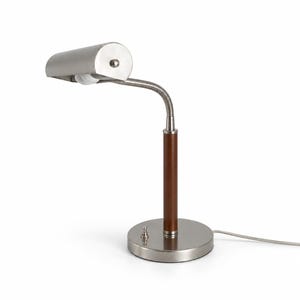 May include: A desk lamp with a brushed nickel finish, featuring a cylindrical head, a flexible gooseneck arm, and a central post wrapped in brown leather. The lamp has a round base with a small silver push-button switch and a thin power cord.