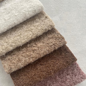 May include: A collection of five rectangular fabric swatches arranged in a diagonal stack. The textures are thick, curly, and looped, featuring a gradient of colors ranging from off-white to light beige, medium brown, dark brown, and dusty rose.