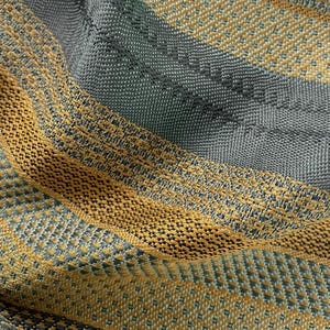 May include: A close-up view of a woven textile featuring a repeating pattern of alternating diagonal stripes in mustard yellow and slate gray. The fabric displays a distinct, textured grid-like weave structure with visible interlaced threads.