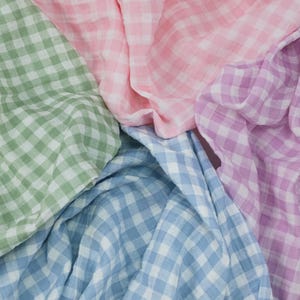 May include: A collection of soft, lightweight fabric pieces featuring a classic gingham check pattern. The textile assortment includes four distinct pastel colors: sage green, light pink, lavender, and sky blue, all arranged in overlapping folds.