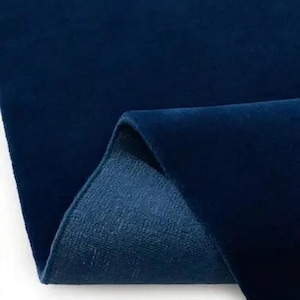 May include: A deep navy blue velvet fabric with a soft, dense pile and a smooth, reflective surface. The material is folded over to reveal the textured, matte underside, showcasing the contrast between the plush top and the woven backing.
