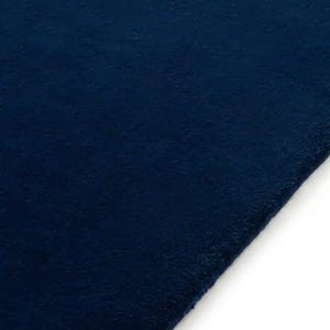 May include: A solid dark navy blue rug with a dense, short-pile texture. The rectangular textile features a clean, straight edge along the right side, showcasing a uniform deep blue color throughout the entire surface of the fabric material.