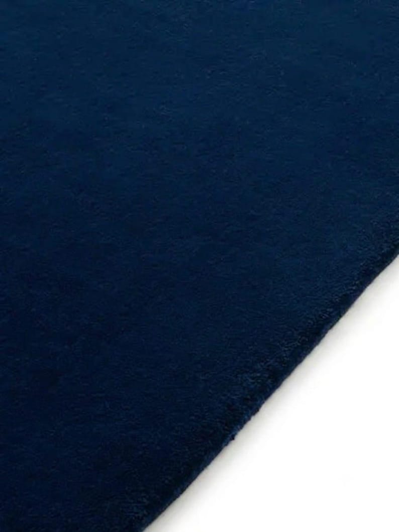 May include: A solid dark navy blue rug with a dense, short-pile texture. The rectangular textile features a clean, straight edge along the right side, showcasing a uniform deep blue color throughout the entire surface of the fabric material.