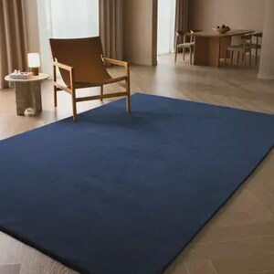 May include: A large, rectangular area rug in a solid, deep navy blue color. The rug features a smooth, uniform texture and is laid flat on a light-colored wooden floor, covering a significant portion of the visible floor space in the room.