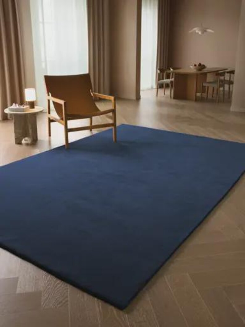 May include: A large, rectangular area rug in a solid, deep navy blue color. The rug features a smooth, uniform texture and is laid flat on a light-colored wooden floor, covering a significant portion of the visible floor space in the room.