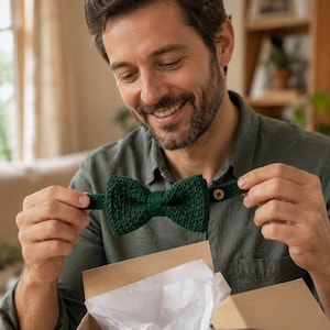 May include: A dark forest green knitted bow tie featuring a textured, woven fabric construction. The bow tie includes an adjustable strap with a small, round, light brown wooden button detail for fastening, presented in a simple style.
