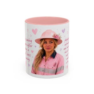 May include: A white ceramic mug with a pink interior rim featuring a photographic print of a person wearing a pink hard hat with flowers, a pink button-down shirt, and text in pink script. The design includes small pink and purple heart illustrations.