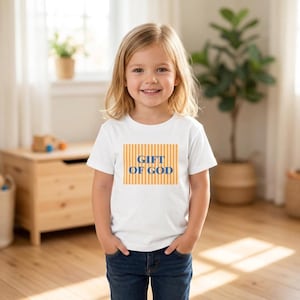 Op de afbeelding: Een wit T-shirt met korte mouwen en een rechthoekige afbeelding met verticale oranje strepen, met de tekst "GIFT OF GOD" in dikke blauwe hoofdletters in het midden van het ontwerp.