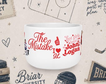 Könnte beinhalten: Ein weißer Keramikbecher mit roter und rosa Grafikschrift und Illustrationen. Der Text lautet The Mistake, I heart JL und hot girls love John Logan. Zudem ist eine kleine rote Schaumstoffhand mit I FAN 22 sowie ein Eishockeyspieler abgebildet.