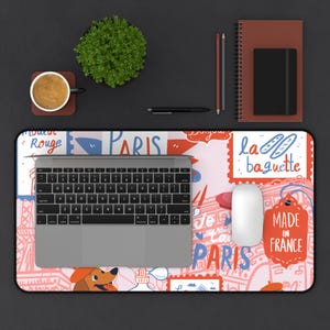 May include: A rectangular desk mat featuring a colorful Paris-themed illustration with text including Paris, Moulin Rouge, Bonjour, la baguette, Je t'aime, and Made in France, with a silver laptop and a white computer mouse placed on top.