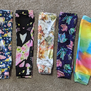 May include: Six pairs of colorful leggings with different patterns. The patterns include unicorns, cats, animals, crystals, and tie-dye.