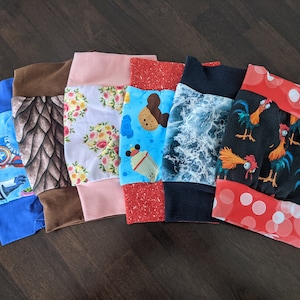 Puede incluir: Siete retazos de tela diferentes con varios patrones coloridos. Los patrones incluyen un patrón azul y blanco con un superhéroe, un patrón marrón y negro con un dinosaurio, un patrón blanco y rosa con flores, un patrón azul y rojo con un personaje de dibujos animados, un patrón azul y blanco con olas, un patrón rojo y blanco con lunares y un patrón negro y verde con un gallo.