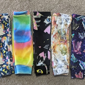 May include: Five pairs of colorful leggings with different patterns. The patterns include unicorns, rainbows, cats, dinosaurs, and crystals.
