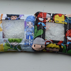 Op de afbeelding: Vier kleine stoffen zakjes met doorzichtige plastic ramen. Elk zakje heeft een ander cartoonpersonage ontwerp. De zakjes zijn blauw, geel, zwart en wit.