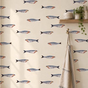May include: Wallpaper featuring a repeating pattern of blue and silver sardines on a cream background. A wooden shelf holds a white bowl and a potted plant with trailing green leaves. A beige apron hangs from a hook on the wall.