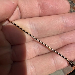 Op de afbeelding: Een dunne goudkleurige metalen brilpoot van een zonnebril. De binnenzijde van de poot is voorzien van een gegraveerde tekst met de tekst RB3025 AVIATOR gevolgd door 58 14. Het metalen oppervlak is glad en reflecterend met een gouden afwerking.