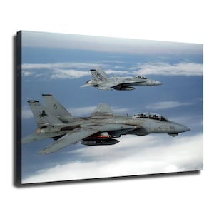 May include: A canvas print featuring two grey fighter jets flying in formation above a layer of clouds. The foreground jet is an F-14 Tomcat with the number 107 visible on its nose, while the background jet is an F/A-18 Hornet. Both aircraft are shown in flight.