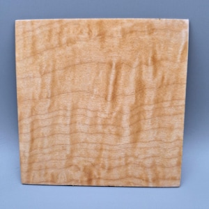 Peut inclure: Une pièce de bois carrée de couleur brun clair présentant un motif de grain ondulé et distinct sur toute la surface. Le bois affiche une coloration naturelle brun doré chaud avec des bandes horizontales de texture de grain plus foncée.