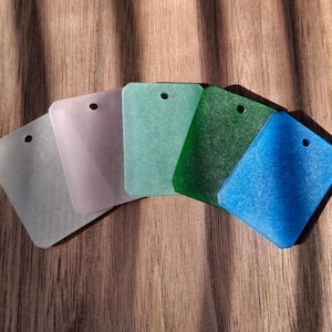 May include: Five rectangular acrylic tags arranged in a fan shape, each featuring a single circular hole at the top. The colours include translucent white, pale lavender, light mint green, deep forest green, and a vibrant, textured blue.
