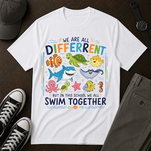 Może przedstawiać: Biały t-shirt z krótkim rękawem z kolorową grafiką przedstawiającą różne stworzenia morskie, w tym rekina, żółwia i ośmiornicę. Tekst głosi: WE ARE ALL DIFFERENT BUT IN THIS SCHOOL WE ALL SWIM TOGETHER. Projekt zawiera niebieskie, zielone i żółte akcenty.
