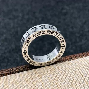 K&ouml;nnte beinhalten: Ein silberfarbener Metallring mit der eingravierten Aufschrift CHROME HEARTS auf dem &auml;u&szlig;eren Band, unterbrochen von kleinen Kreuzsymbolen. Die Innenseite des Rings zeigt die Gravuren 2003 und .925, die das Jahr und die Metallreinheit angeben.
