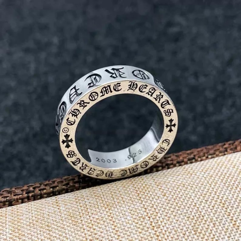 K&ouml;nnte beinhalten: Ein silberfarbener Metallring mit der eingravierten Aufschrift CHROME HEARTS auf dem &auml;u&szlig;eren Band, unterbrochen von kleinen Kreuzsymbolen. Die Innenseite des Rings zeigt die Gravuren 2003 und .925, die das Jahr und die Metallreinheit angeben.