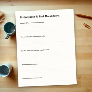 Op de afbeelding: Een wit papieren plannerblad met de titel Brain Dump & Task Breakdown met secties voor Dump it all here, The one thing that matters most today, Break it down, Waiting on someone else en Parking lot: not now, not never met lijnen.