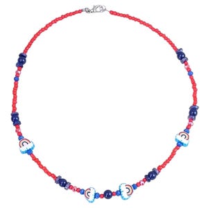 Peut inclure: Un collier de perles composé d'un cordon de petites perles rouges alternées avec des perles sphériques bleu foncé plus grandes et trois breloques blanches, chacune ornée d'un motif arc-en-ciel coloré, fermé par un fermoir en métal argenté.