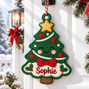 May include: A felt Christmas tree ornament featuring a smiling face, a yellow star topper, red circular ornaments, and a red bow tie. The base is white with the name Sophie embroidered in red script, accented by green holly leaves and red berries.