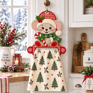 Può includere: Un portasciugamani da cucina sospeso con un topo di peluche che indossa un cappello a quadretti rossi e bianchi e una sciarpa a quadri verdi, mentre tiene un bastoncino di zucchero. L'asciugamano color crema ha un motivo di alberi di Natale.