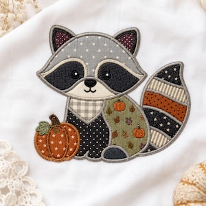 May include: A fabric applique of a raccoon featuring a gray star-patterned head, black eye patches, and a striped tail. The body includes a black polka-dot chest, a green section with pumpkin and leaf prints, and a separate orange star-patterned pumpkin.